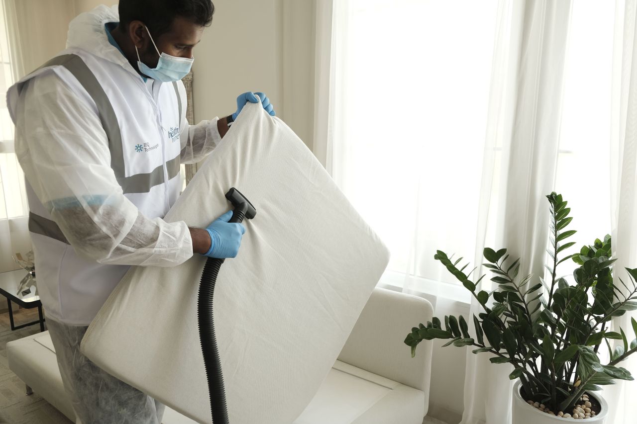 about-01 Man in protective gear vacuuming a mattress in a modern home interior.